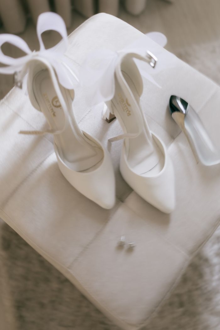 Close-up of elegant white bridal shoes with ribbon bows over a soft background.